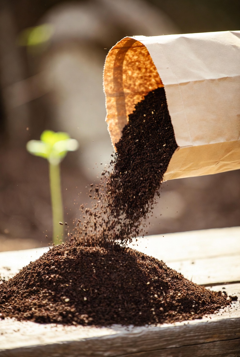 Dark potting soil pouring from a kraft bag onto a wooden table